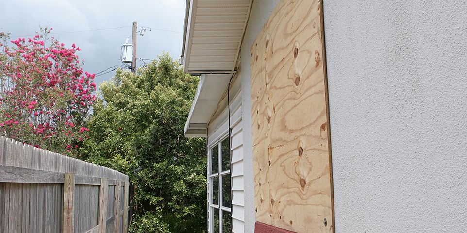 A home with plywood covering the window in preparation for a hurricane.  The storm clouds are gathering in the sky.  Horizontal view.
